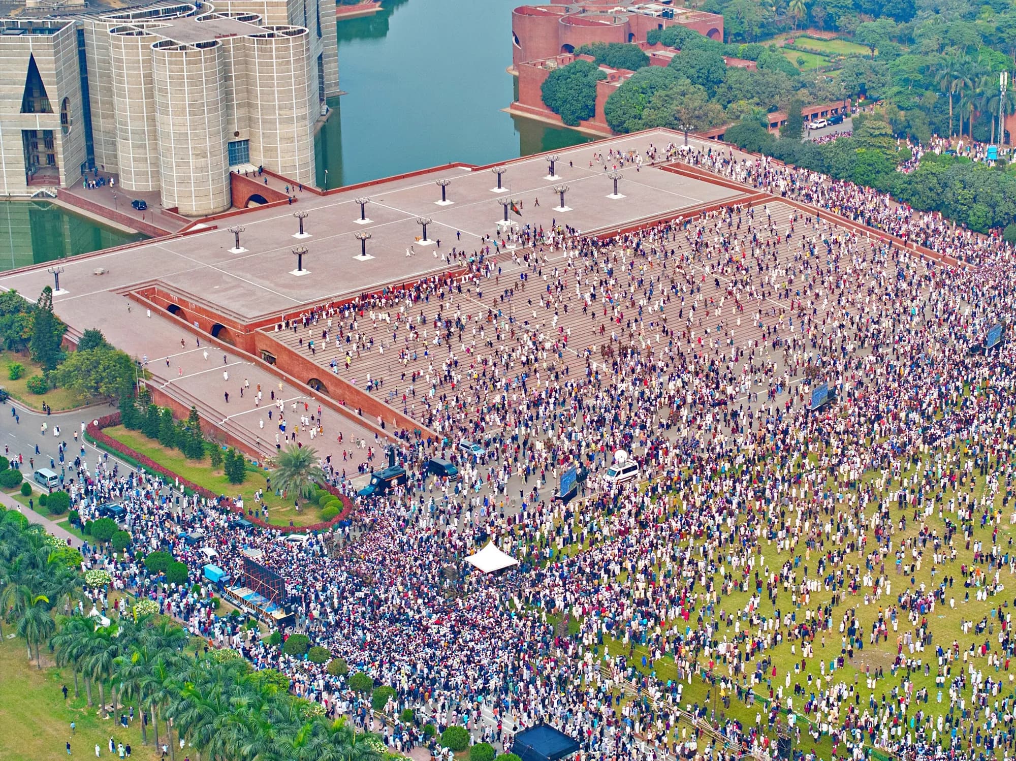 Aerial view of a vast crowd covering a brick plaza and the lawns beside it, with the concrete parliament building and its lake at the top.