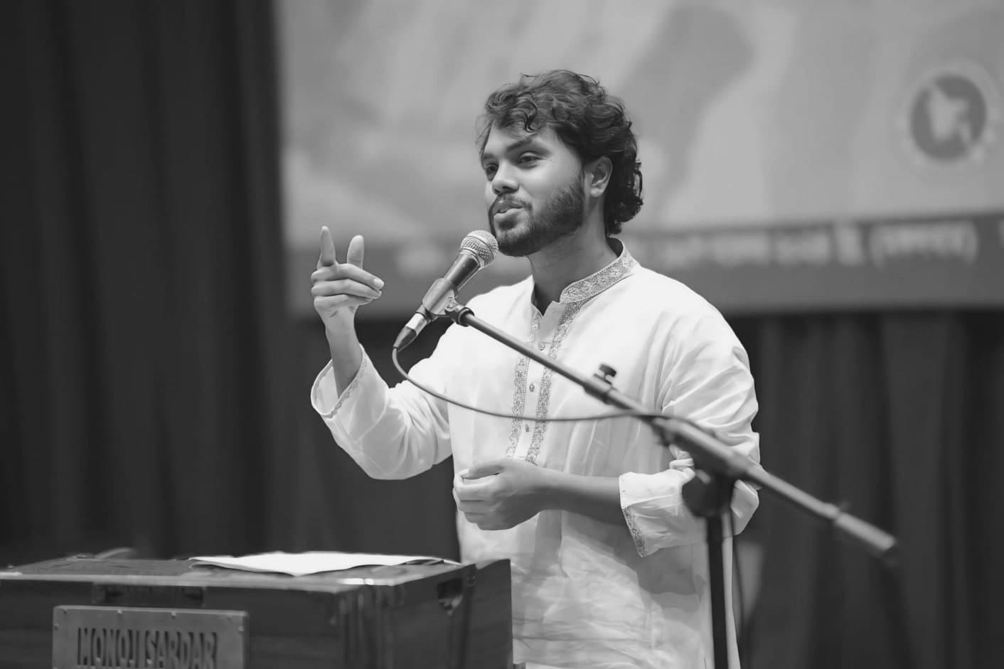Sharif Osman bin Hadi in a white panjabi, speaking into a microphone on a stage and gesturing with one hand.